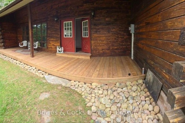 Wooden deck curves around the side of the log home. - 82 Bay Lake Road, Bancroft