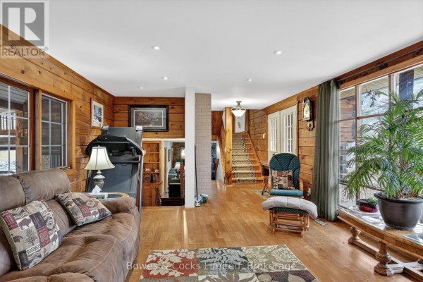 Living room with wood paneling, sofa, treadmill, rocking chair, and large window - 82 Bay Lake Road Bancroft