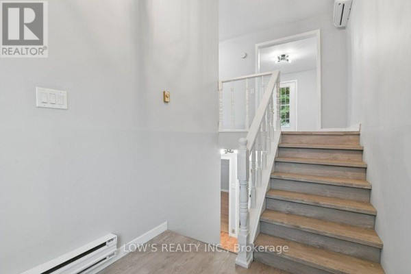 Interior hallway with a light grey staircase, white banister, and wood-look laminate flooring. - 82 Bertha Street, Champlain