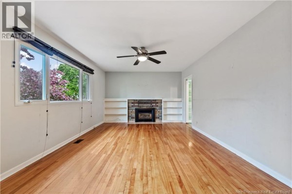 Empty living room with hardwood floors, a fireplace, built-in shelves, and a ceiling fan. - 82 Eighth Street, Moncton
