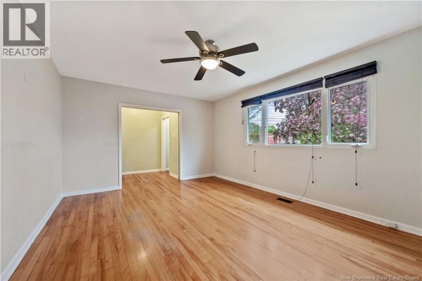 View of a spacious room with hardwood floors, a ceiling fan, and a large window. - 82 Eighth Street, Moncton