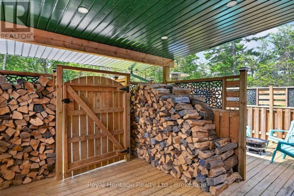 Covered wooden deck area with stacked firewood, gate, and teal chairs. - 82 Kennedy Drive, Trent Lakes