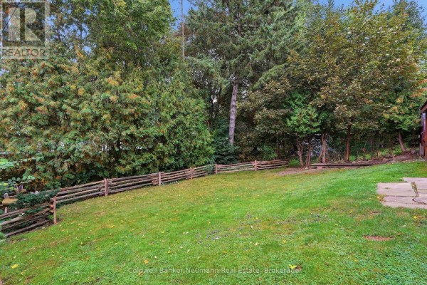 Backyard with a wooden fence, green grass, and mature trees. - 82 Knightswood Boulevard, Guelph