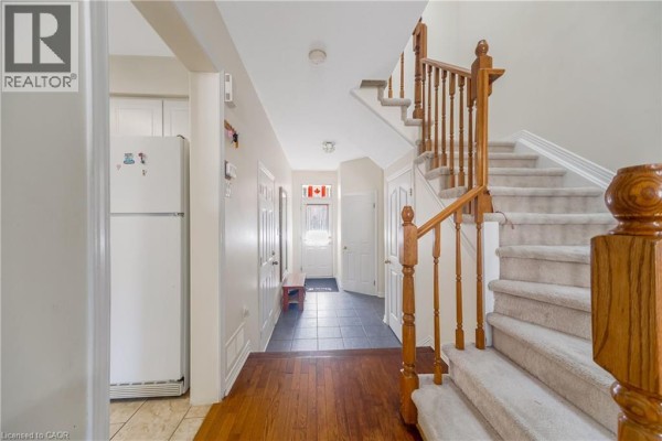 Hallway with hardwood floors, dark tiled floor, and carpeted staircase. - 82 Milner Downs Crescent, Ottawa