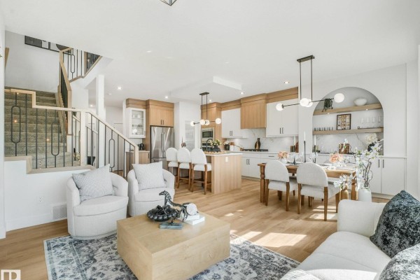 Open concept living area with white furniture, wood floors, carpeted stairs, and kitchen in background. - 82 Ravenshire Wynd, Sherwood Park