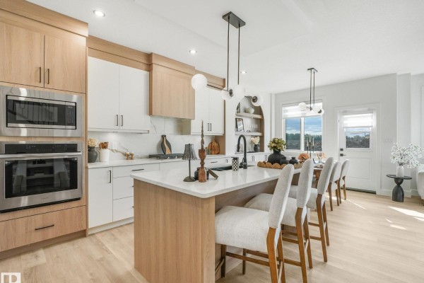 Modern kitchen with two-tone cabinetry, island with bar stools, stainless steel appliances, and large windows. - 82 Ravenshire Wynd, Sherwood Park