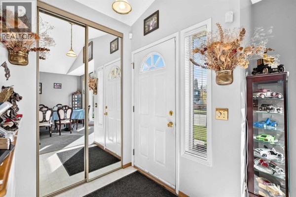 Foyer with mirrored closet doors, a white front door, and display cabinet. - 82 Riverglen Drive Se, Calgary
