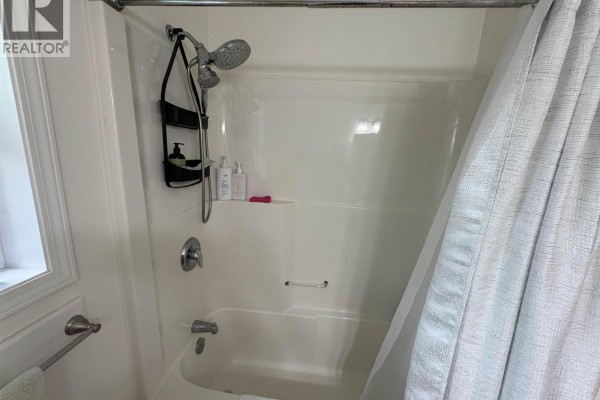 A white bathtub with a handheld showerhead and a grey patterned shower curtain. - 820 Oceanview Drive, Daajing Giids City