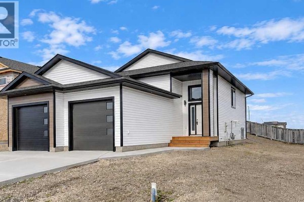 Front view of a white house with a wooden deck, double garage doors, and modern windows. - 8209 87a Street, Grande Prairie