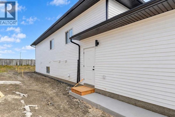 Side view of a white house showing a separate entrance with a wooden step and concrete walkway. - 8209 87a Street, Grande Prairie