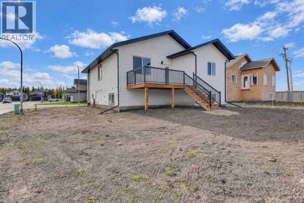 Rear view of a white house with a wooden deck, stairs, and surrounding undeveloped land. - 8209 87a Street, Grande Prairie