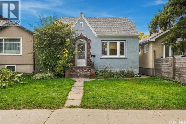 Front exterior of a light blue stucco house with a gabled roof and mature trees. - 821 College Avenue, Regina