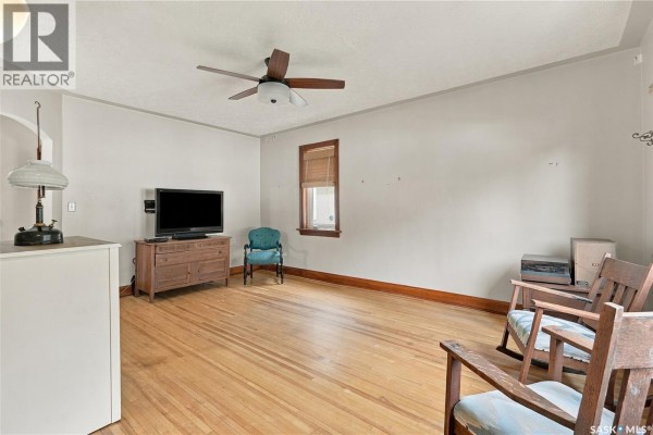 Living room with wood floors, light gray walls, ceiling fan, and wooden furniture. - 821 College Avenue, Regina