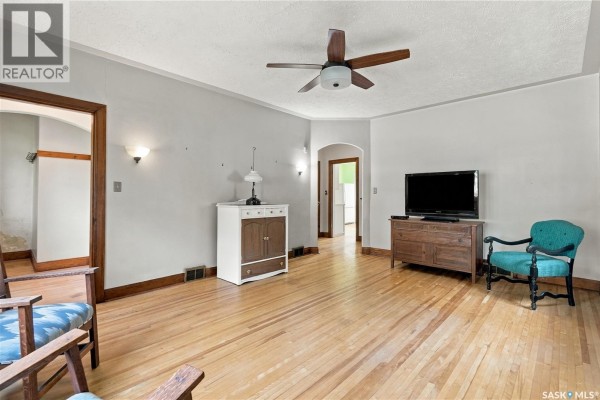 Living room with wood floors, light gray walls, wood furniture, and archways to other rooms. - 821 College Avenue, Regina