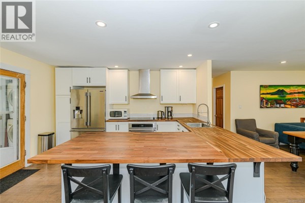 Kitchen with white cabinets, stainless steel appliances, butcher block island, and dining area. - 821 Fulford-ganges Rd, Salt Spring