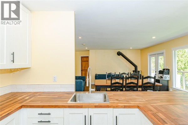 Kitchen island with sink, white cabinets, and a view of the dining area with a wood stove. - 821 Fulford-ganges Rd, Salt Spring