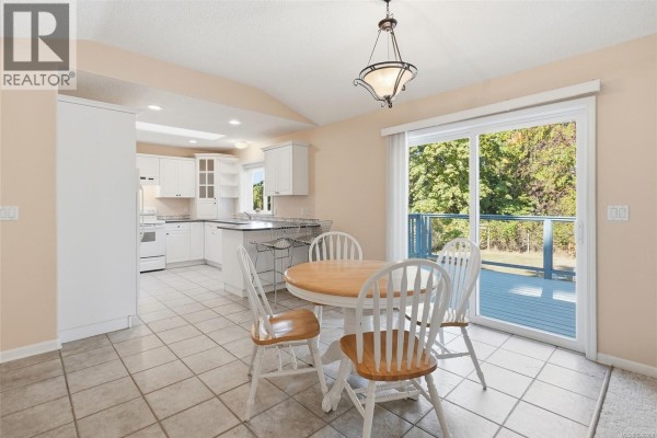 Dining area with a round wooden table and chairs, adjacent to a sliding glass door with a deck view. - 821 Shorewood Dr, Parksville