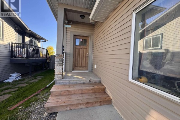 Living room and kitchen area with dark cabinets, stainless steel appliances, and a large grey sectional sofa. - 8211 96 Avenue, Fort St  John