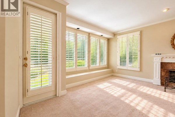 Empty living room with beige carpet, white plantation shutters on windows, and a door leading outside. - 8211 Tugboat Place, Vancouver