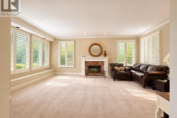 Living room with plush beige carpet, a fireplace with marble surround, and a large leather sectional sofa. - 8211 Tugboat Place, Vancouver