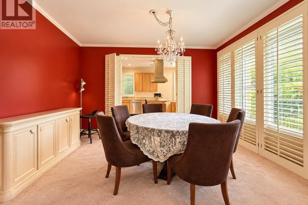 Dining room with a round table set for six, a crystal chandelier, and red walls with white cabinets. - 8211 Tugboat Place, Vancouver