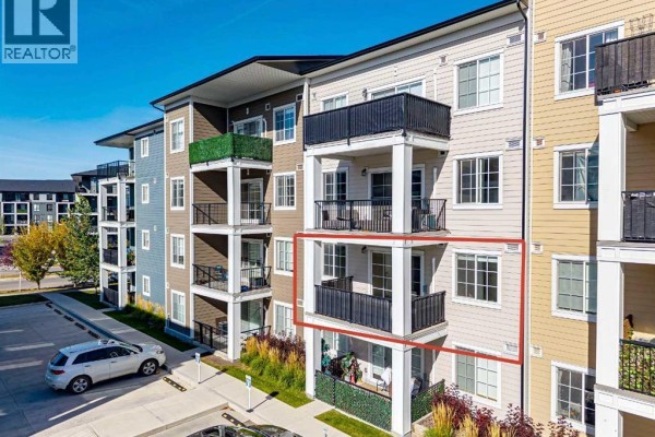 Exterior view of a beige apartment building with balconies, highlighted unit on second floor. - 8216, 151 Legacy Main Street Se, Calgary