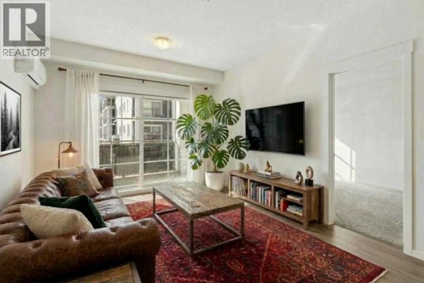 Living room with a brown leather sofa, coffee table, large plant, and window view. - 8216, 151 Legacy Main Street Se, Calgary