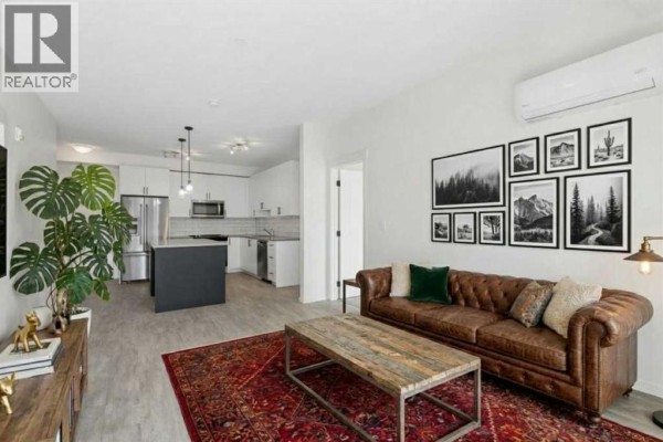 Open concept living room and kitchen with brown leather sofa, coffee table, and island. - 8216, 151 Legacy Main Street Se, Calgary