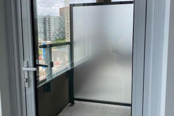 View of a small balcony with frosted glass panels and city buildings through a glass door. - 822 - 270 Dufferin Street, Toronto