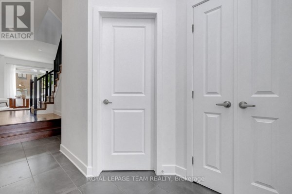 Hallway with grey tile floor, white doors, and stairs with dark wood steps leading to the second floor. - 822 Chipping Circle, Ottawa