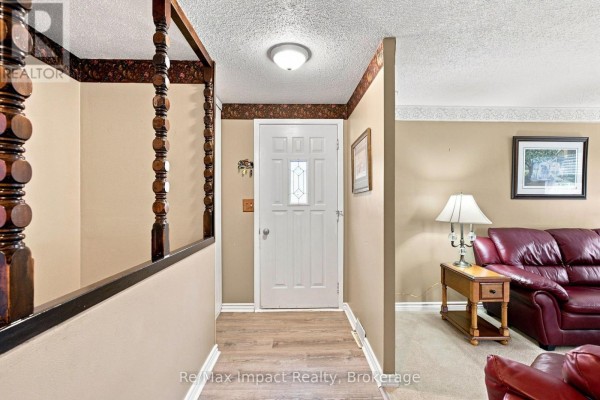 Interior entryway with a white door, beige walls, and a view into a living room with a leather couch. - 822 Southdown Street, Oshawa