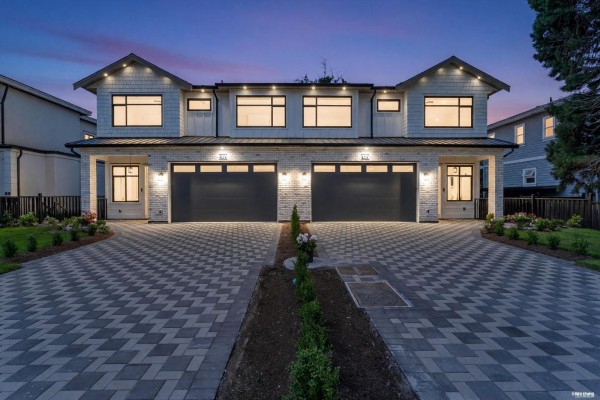 Front exterior of a duplex with modern architecture, two garages, and manicured lawns. - 8221 111b Street, Delta