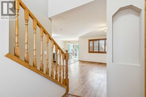 View from the entrance looking towards the living room and kitchen, featuring a wooden staircase and railing. - 8226 Saddleridge Drive Ne, Calgary