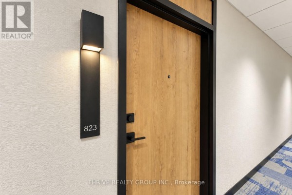 Apartment door number 823 with a modern black light fixture and textured wall. - 823 - 100 Fullarton Street, London East