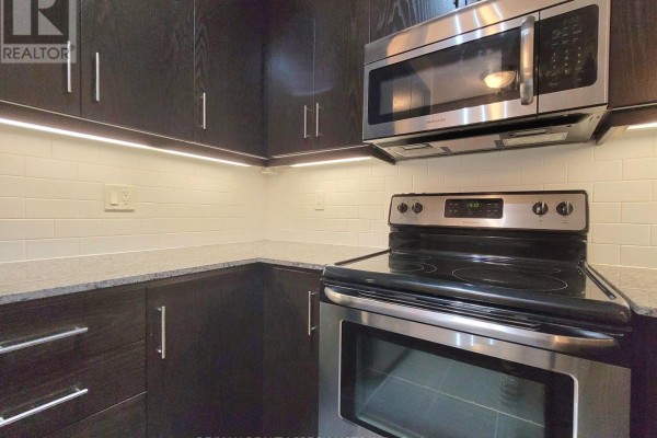 Living and dining area with dark wood floors and view into the kitchen space. - 823 - 15 James Finlay Way, Toronto