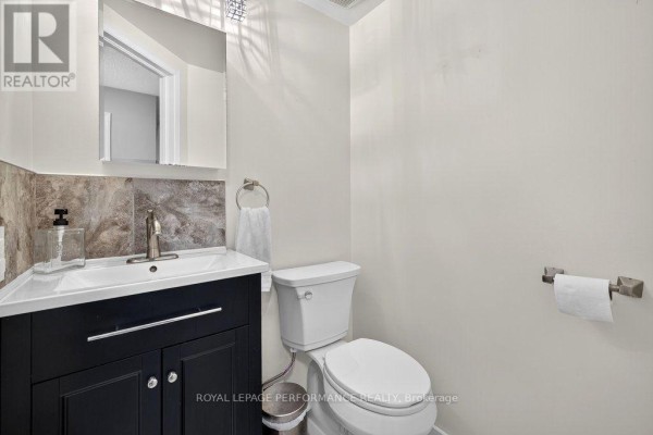 Powder room with a dark vanity, white sink, toilet, and marble backsplash. - 823 Nesting Way, Ottawa