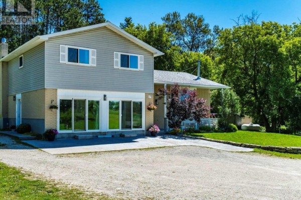 Close-up side view of the house with a white porch, red-brick base, and large glass doors. - 8231 56 County Road, Essa