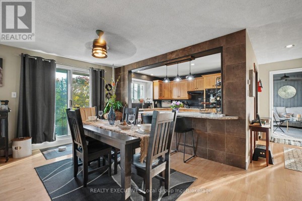 Dining area with dark wood table and chairs, open to a kitchen with light wood cabinets. - 824 Ski Club Road, North Bay