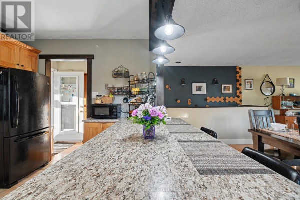 Kitchen island with speckled granite countertop and pendant lights, overlooking a dining area. - 824 Ski Club Road, North Bay