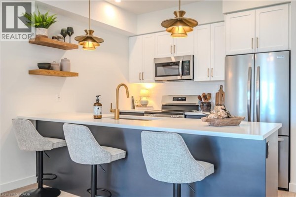 Kitchen island with three bar stools and stainless steel appliances. - 824 Woolwich Street Unit# 66, Guelph