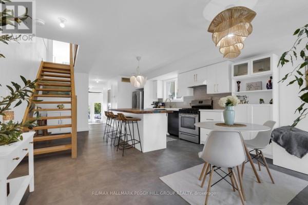 Open-concept living space with a white kitchen, dining area, and a wooden staircase. - 825 Adams Road, Innisfil