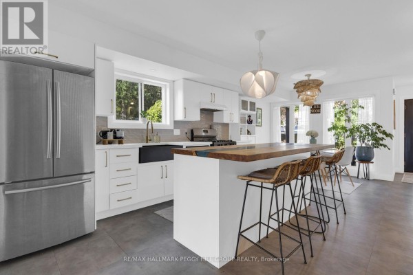 White kitchen featuring stainless steel appliances, a wooden island with stools, and a window. - 825 Adams Road, Innisfil
