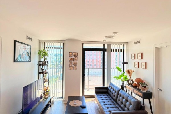 Living room showing a dark grey tufted sofa, console table, and large windows with city views. - 827 - 1 Jarvis Street, Hamilton