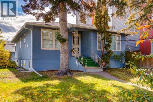 Side exterior view of a blue bungalow with white trim, showing the foundation and a window well. - 827 17 Avenue Nw, Calgary