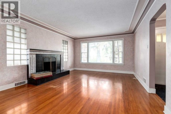 Living room with hardwood floors, a black fireplace with a tiled surround, and a large window. - 827 17 Avenue Nw, Calgary