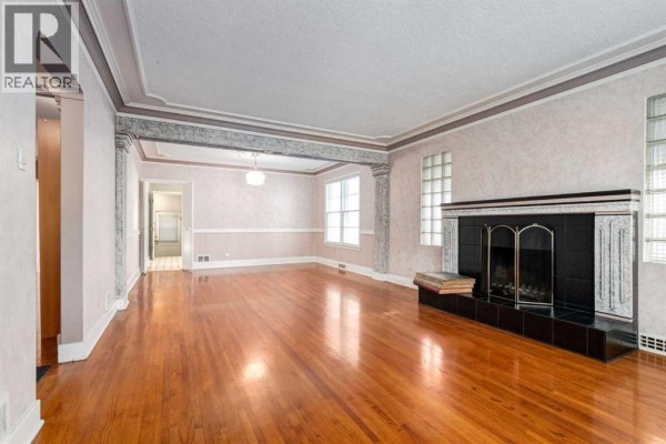 Living room with hardwood floors, a decorative fireplace, glass block windows, and an arched doorway. - 827 17 Avenue Nw, Calgary
