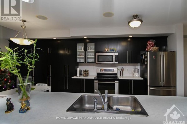Modern kitchen with black cabinets, stainless steel appliances, and a large double sink. - 829 Percifor Way, Ottawa