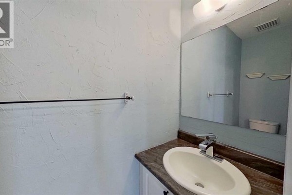 Powder room with light blue textured walls, vanity, sink, and mirror. - 83, 1055 72 Avenue Nw, Calgary