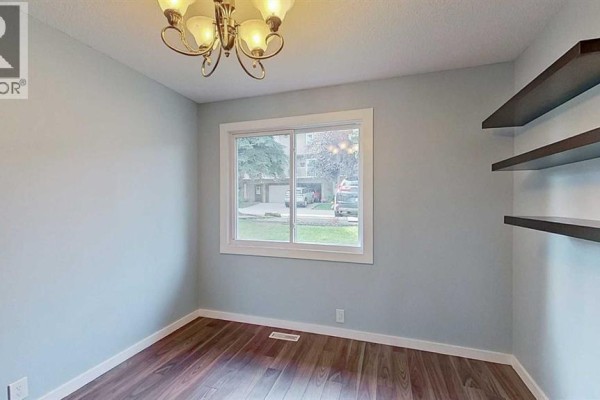 Empty room with light blue walls, wood floor, and a sliding window. - 83, 1055 72 Avenue Nw, Calgary