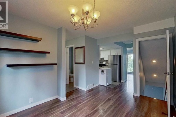 Dining area with wood floor, light blue walls, kitchen, and stairs. - 83, 1055 72 Avenue Nw, Calgary